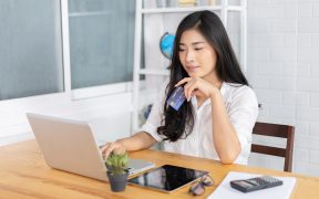 Image of a young woman sitting at her computer online shopping holding a credit card in her hand for E-commerce in Asia Growth of the Online Marketplace blog post